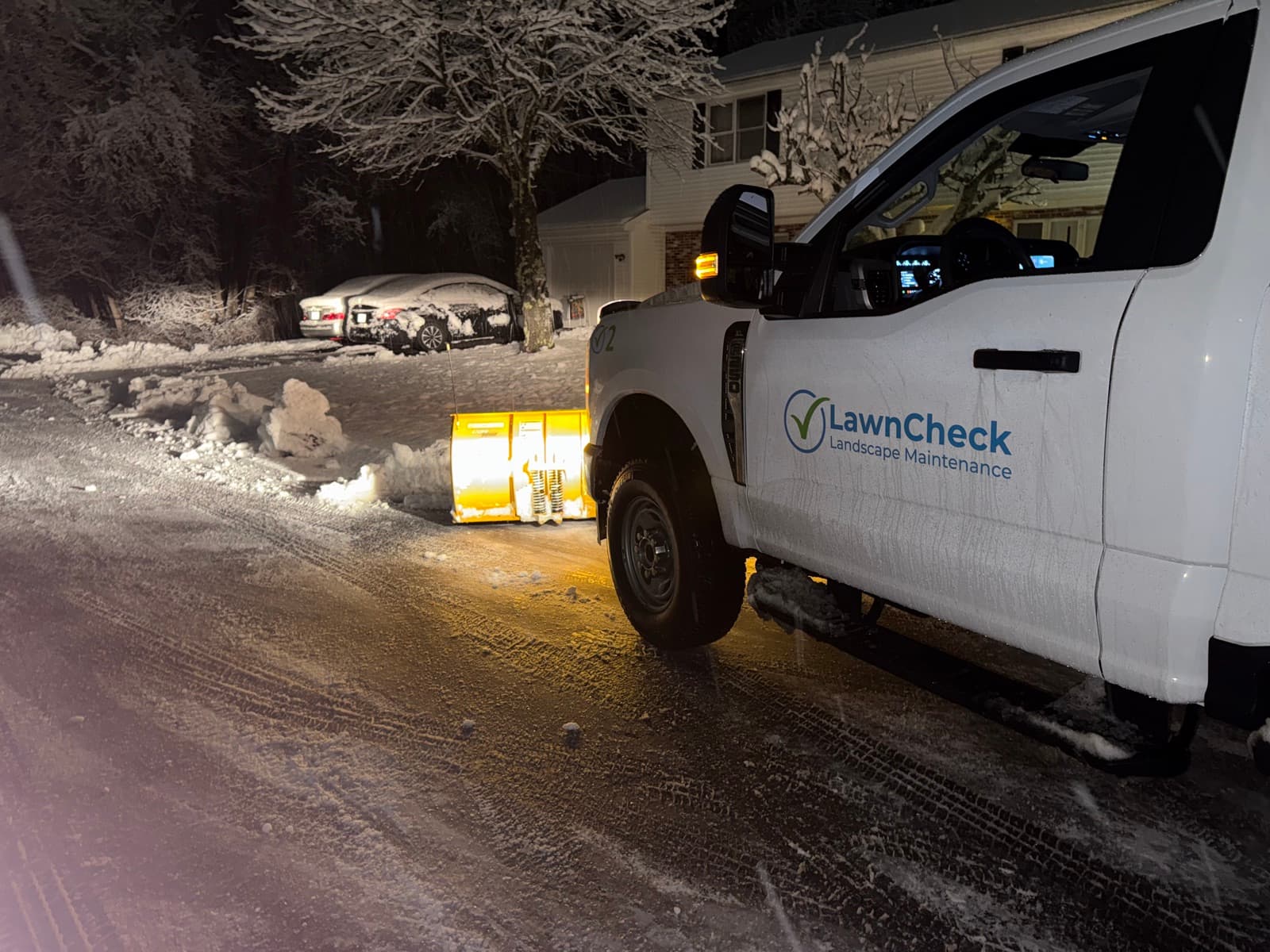 The LawnCheck truck plowing a residential street during a snowstorm