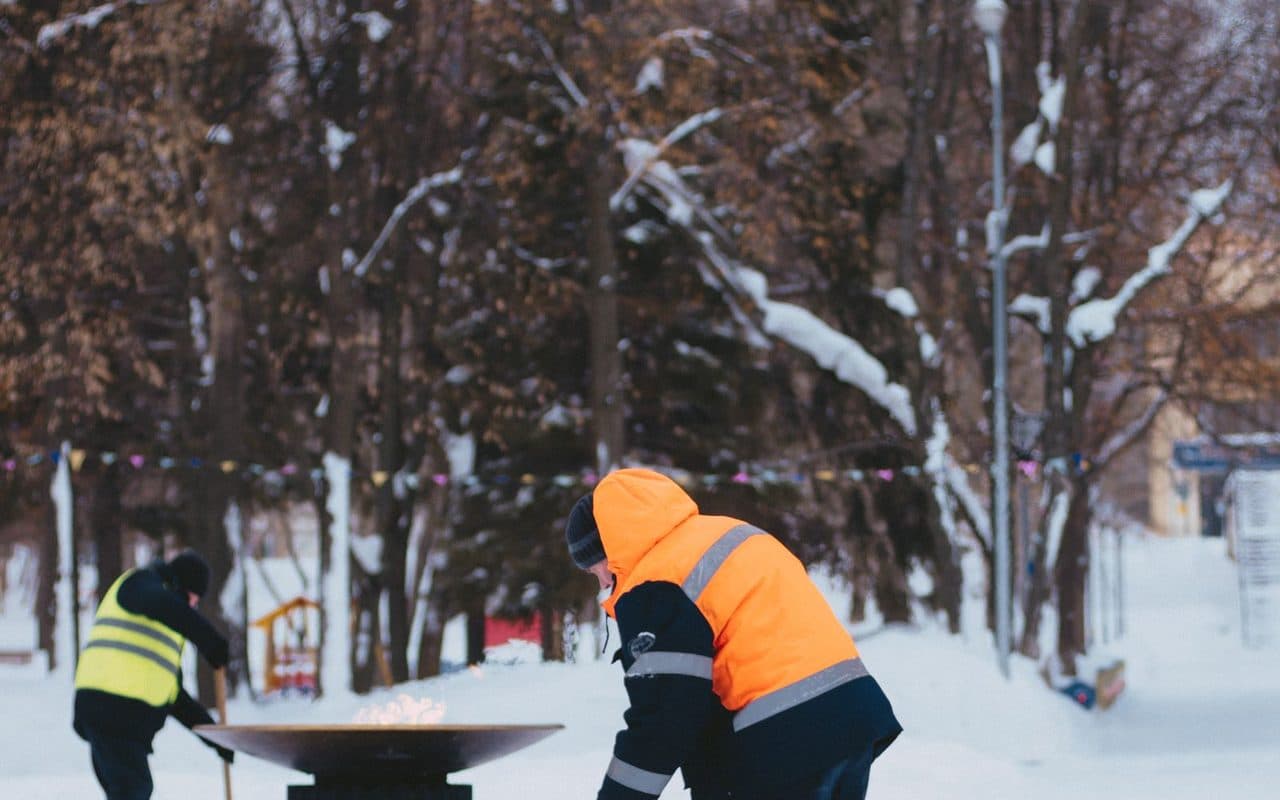 A crew in winter gear clearing snow from a walkway by hand