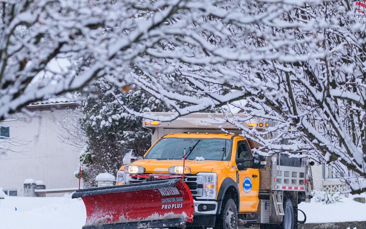 A plow truck clearing a snow-covered residential street after a storm