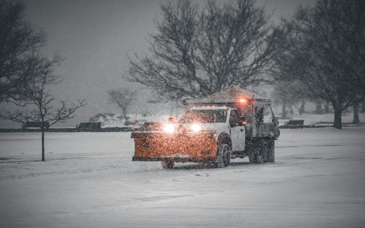 A plow truck pushing through heavy falling snow during an active storm