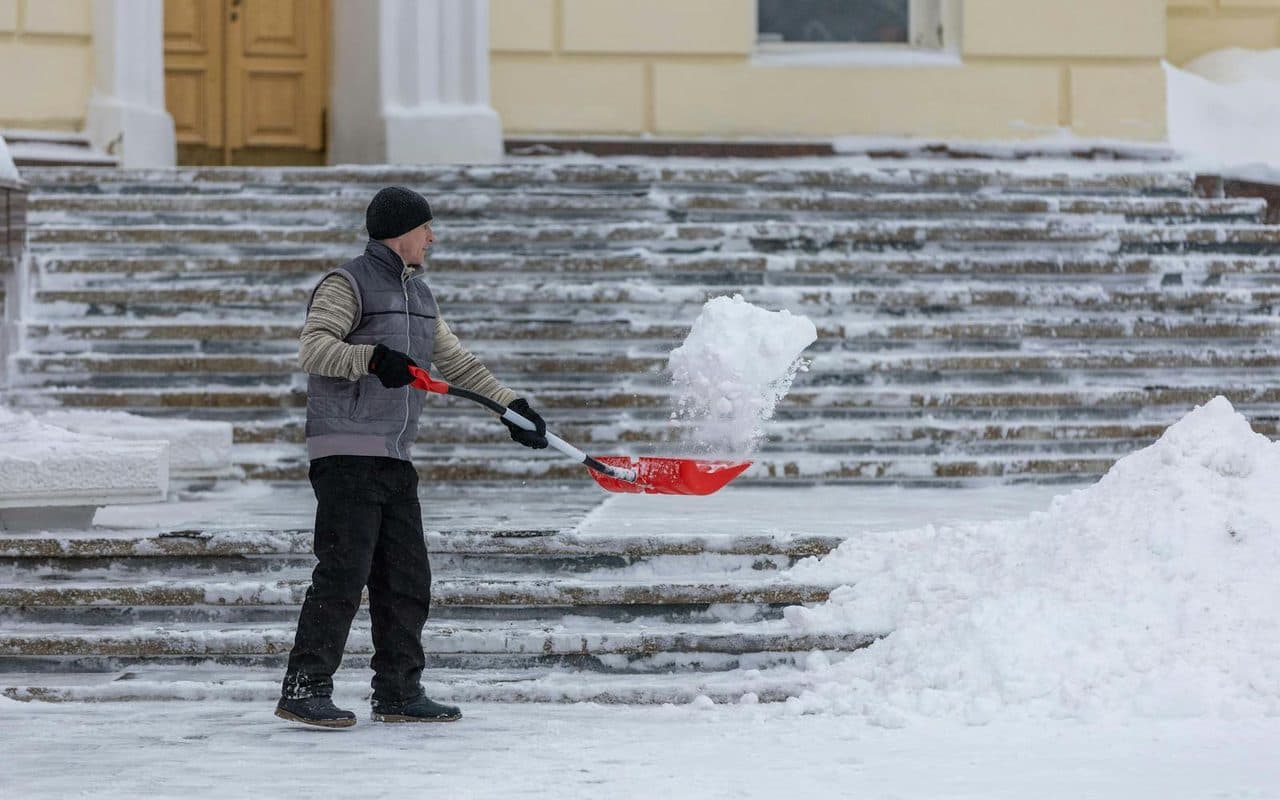 A worker shoveling snow from a sidewalk outside a commercial building