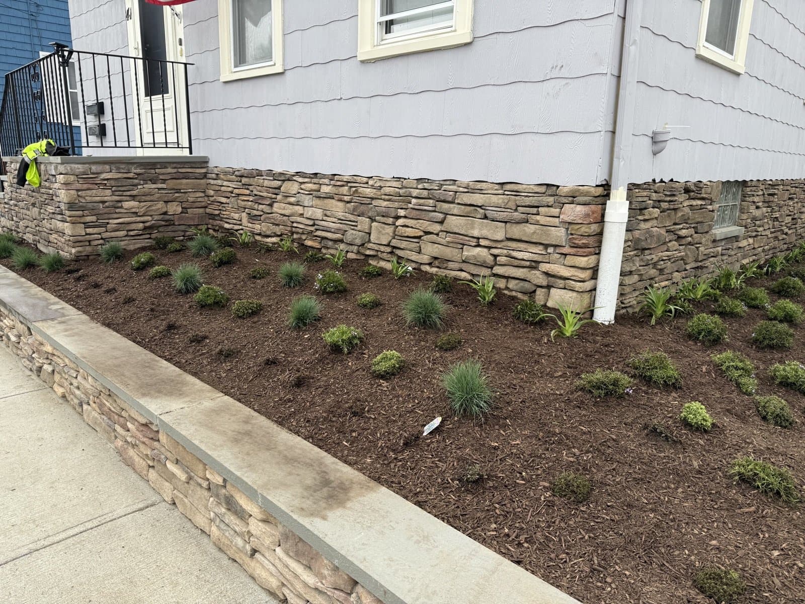 A freshly mulched landscape bed with new plantings along a stone property wall