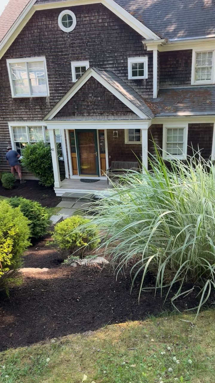 A long, freshly mulched and cleaned planting bed beside a manicured lawn at a waterfront property in Portsmouth