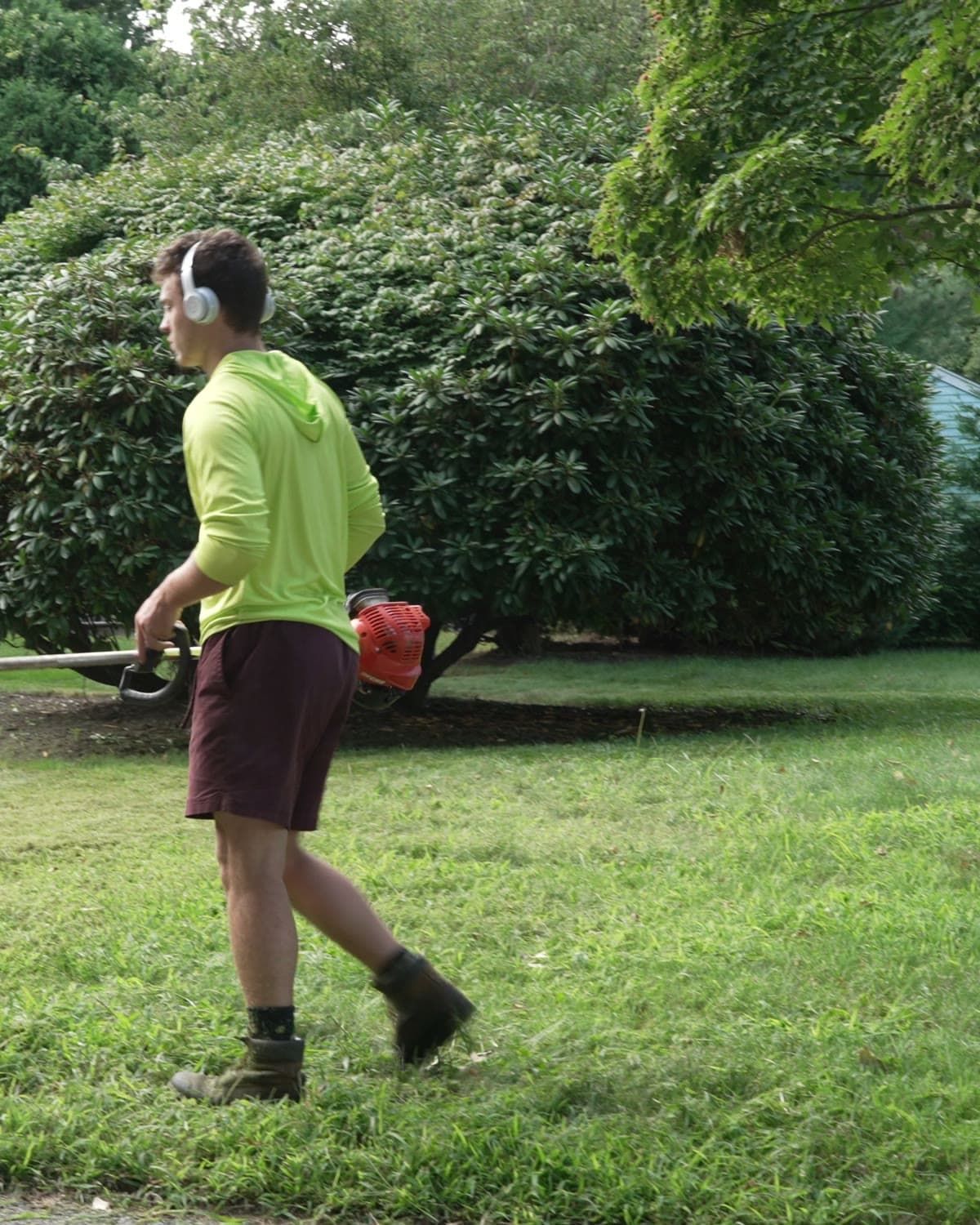 A crew member trimming shrubs beside a house