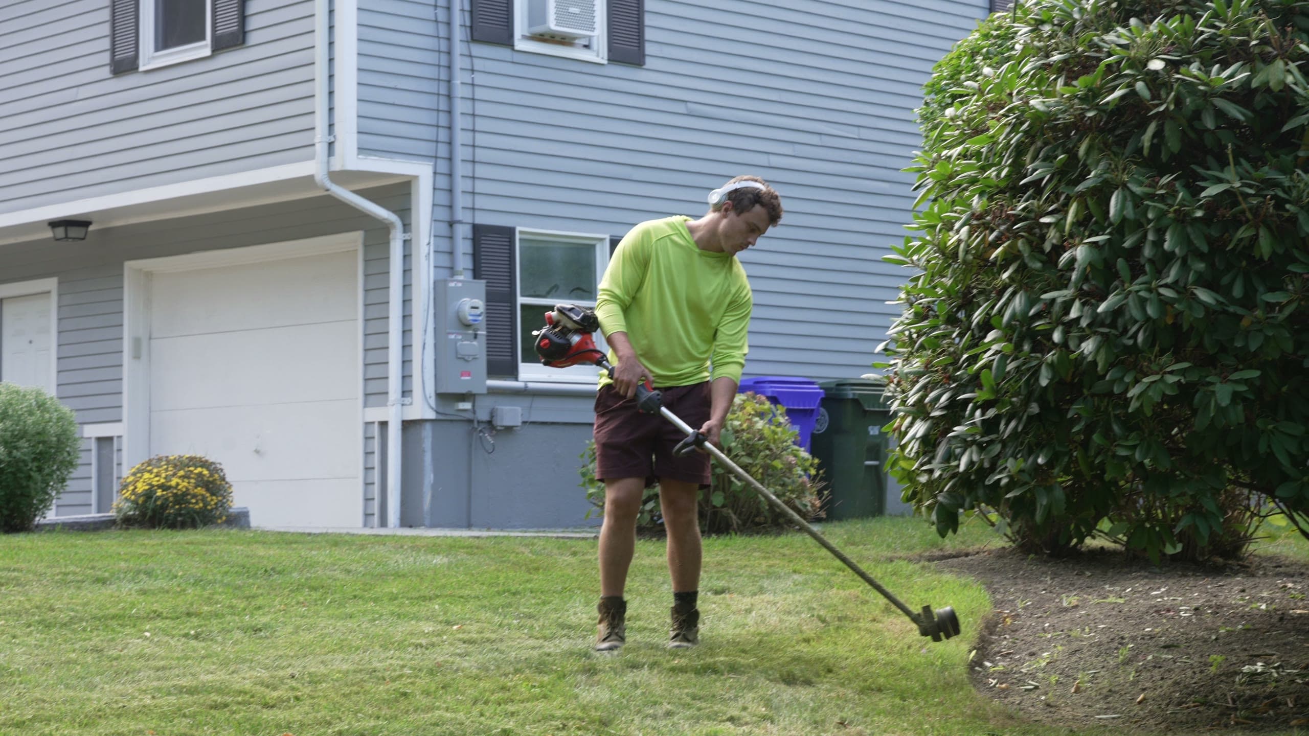 A crew member trimming along a bed in front of a house