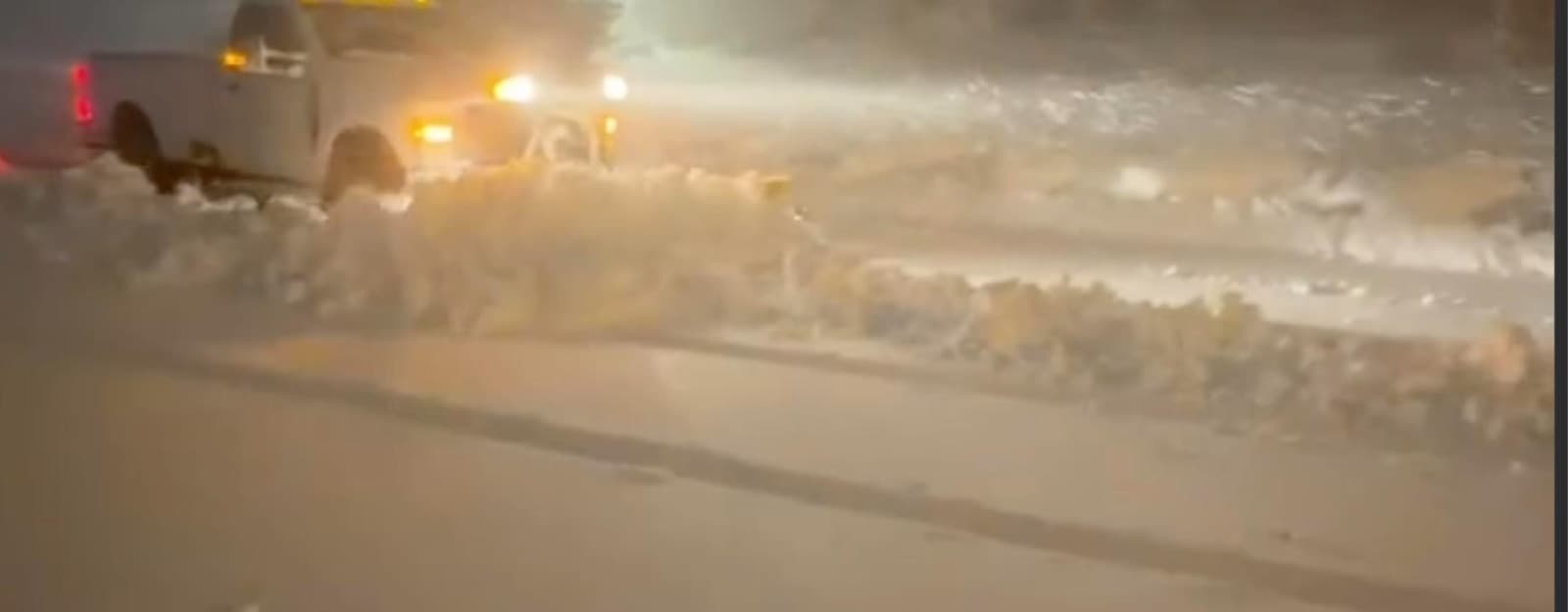 The plow truck pushing snow across a lot at night