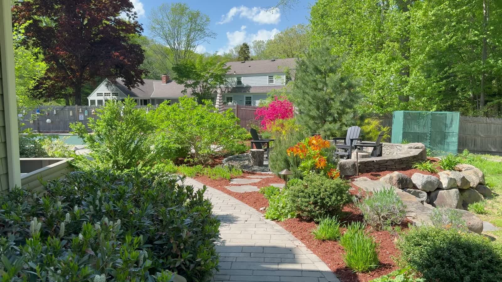 A LawnCheck-built backyard in the East Bay — stone walkway, fresh mulch beds, blooming azaleas, and a fire pit